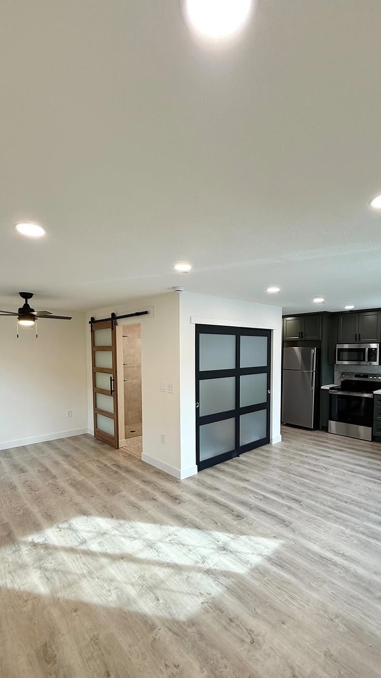 Modern open-concept living space with light wood flooring, sliding barn door, and a dark kitchen.