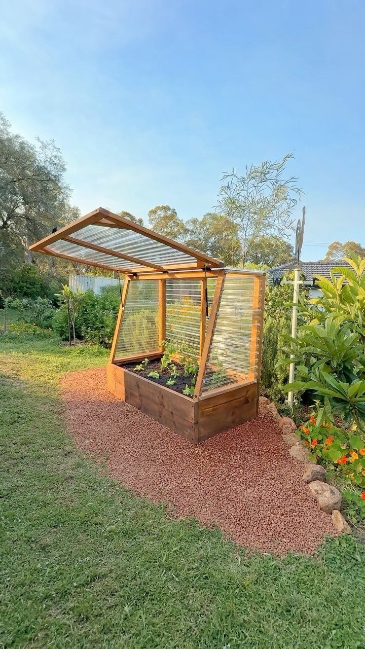 Above Ground Garden Ideas: 12 Ways to Build a Raised Bed 5 A wooden raised garden bed with a translucent greenhouse lid propped open in a backyard garden.
