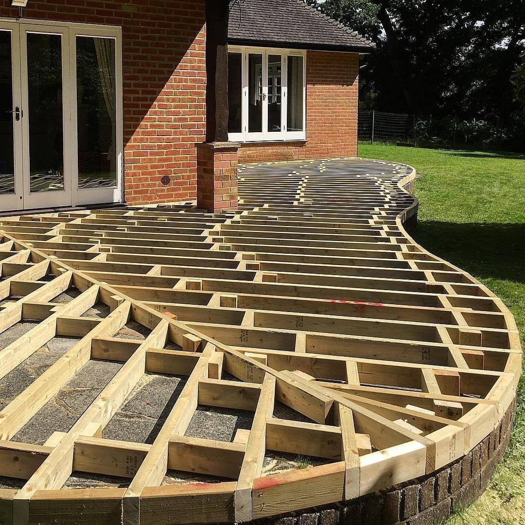 17 Backyard Deck Designs for Every Yard and Budget 16 Wooden deck framing with a curved design being constructed next to a brick house.