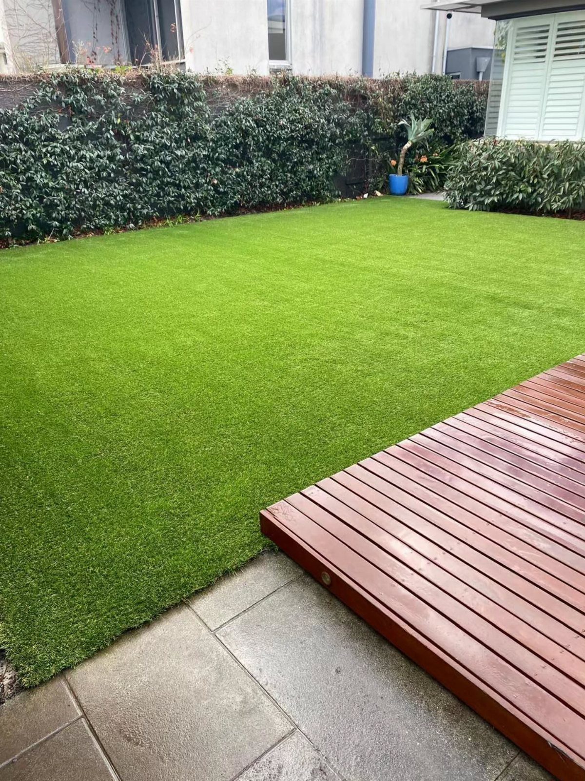 17 Backyard Deck Designs for Every Yard and Budget 6 Wooden deck planks meeting a bright green artificial grass lawn next to stone tiles.