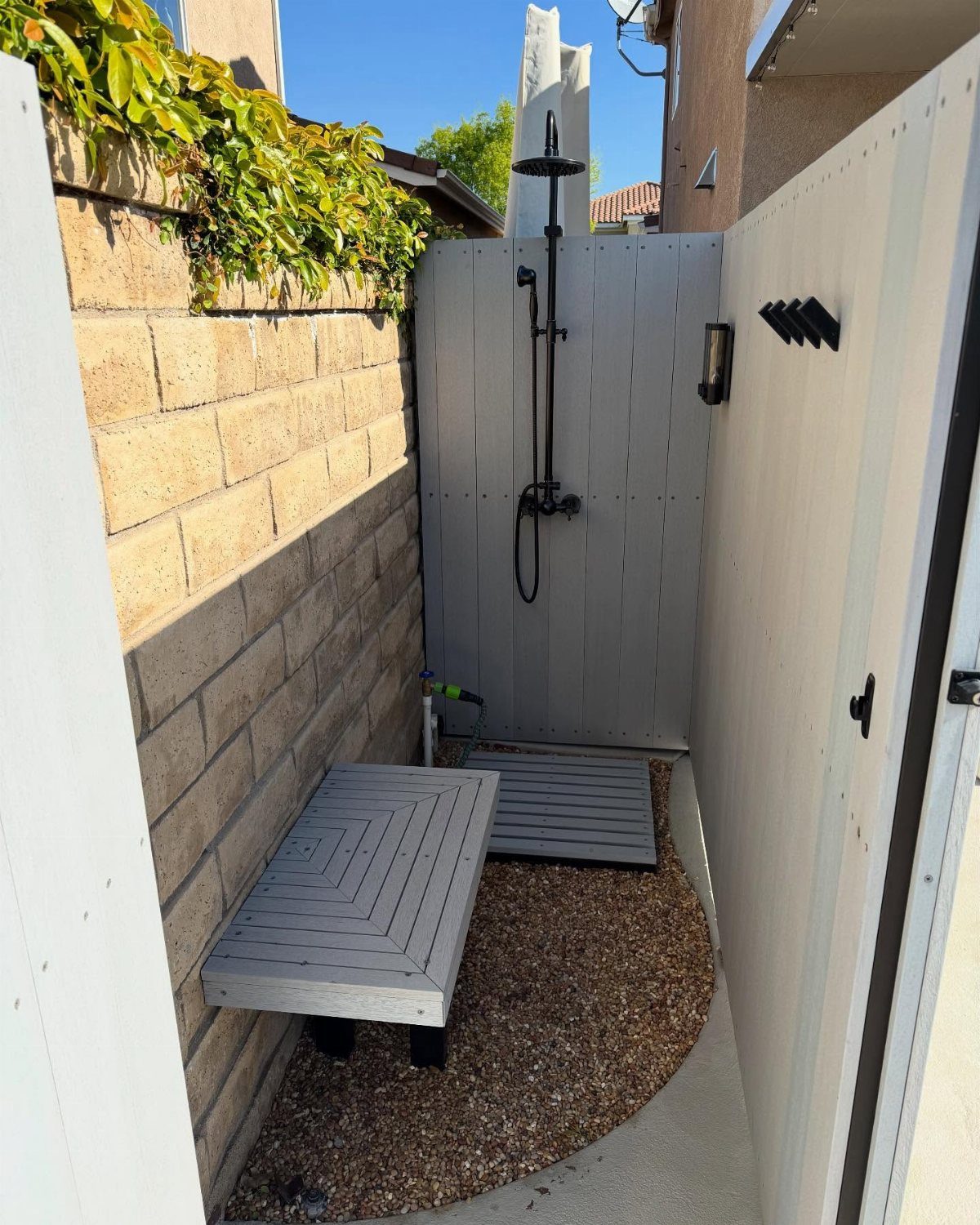 17 Backyard Deck Designs for Every Yard and Budget 7 Grey outdoor shower with black fixtures mounted on a wooden privacy screen next to a bench.