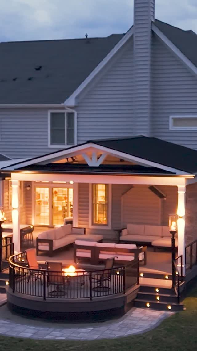 17 Backyard Deck Designs for Every Yard and Budget 10 A multi-level wooden deck with a built-in fire pit and outdoor lounge furniture at dusk.