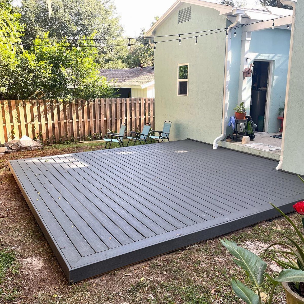 17 Backyard Deck Designs for Every Yard and Budget 1 A dark grey wooden floating deck platform installed on a grassy backyard lawn.