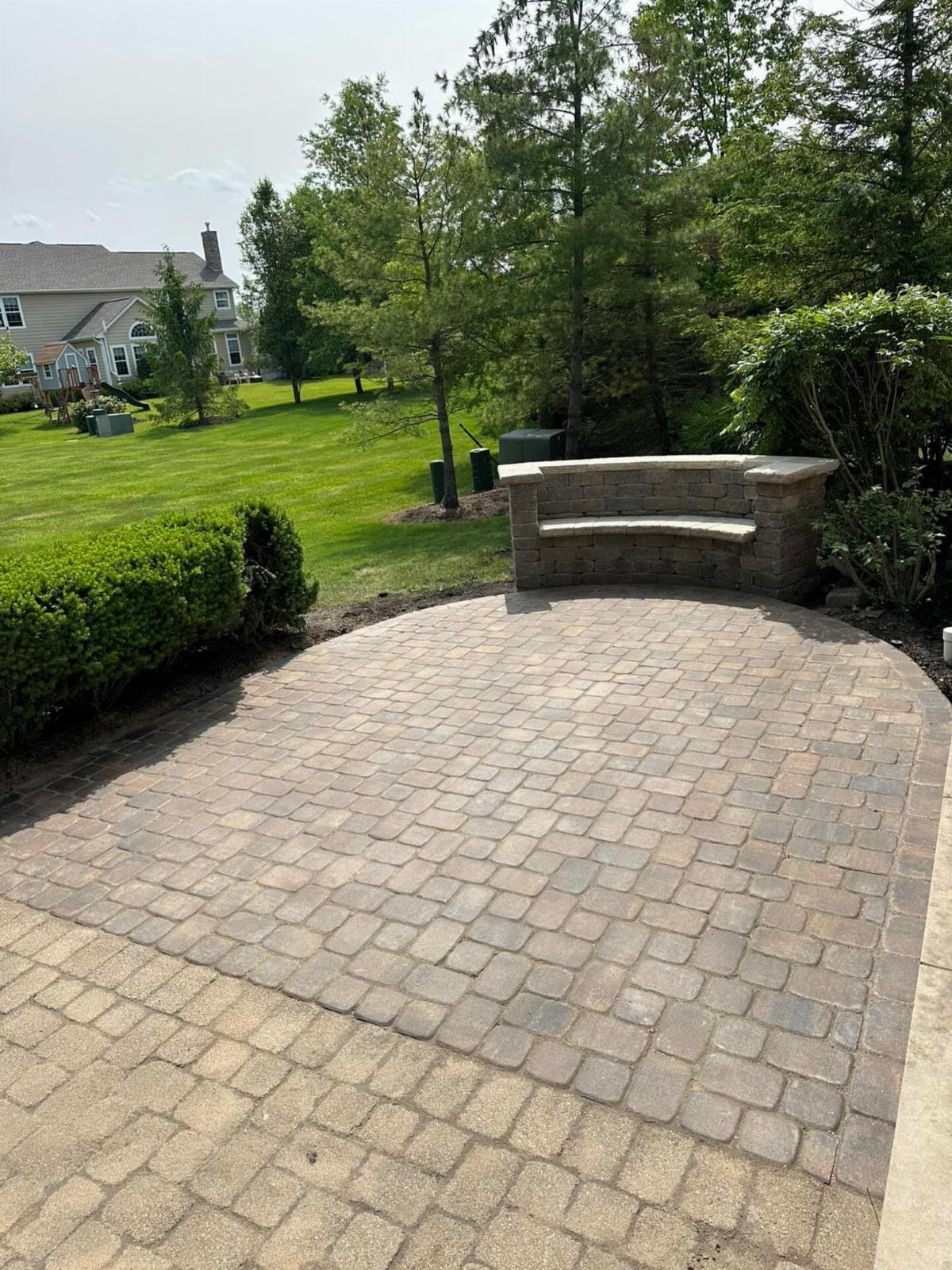 Stone paver patio with a curved built-in stone bench overlooking a green backyard lawn.