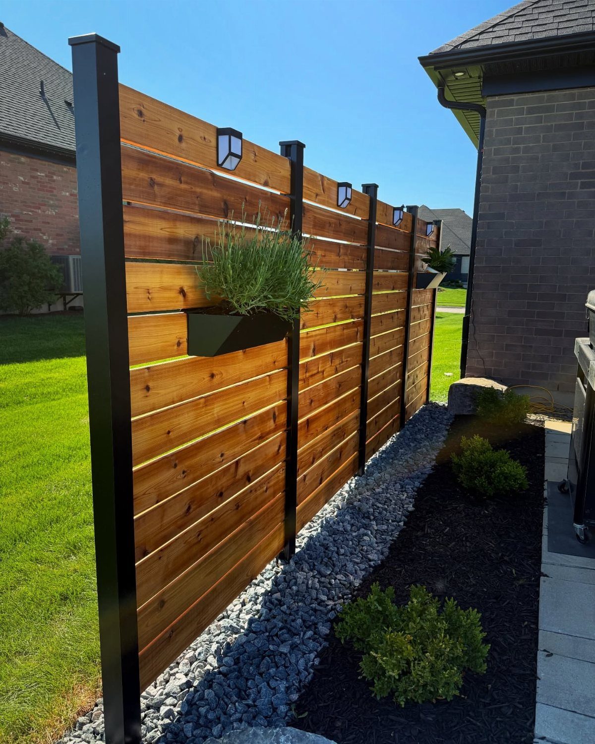 Modern horizontal wooden privacy fence with black metal posts and integrated planters along a garden bed.