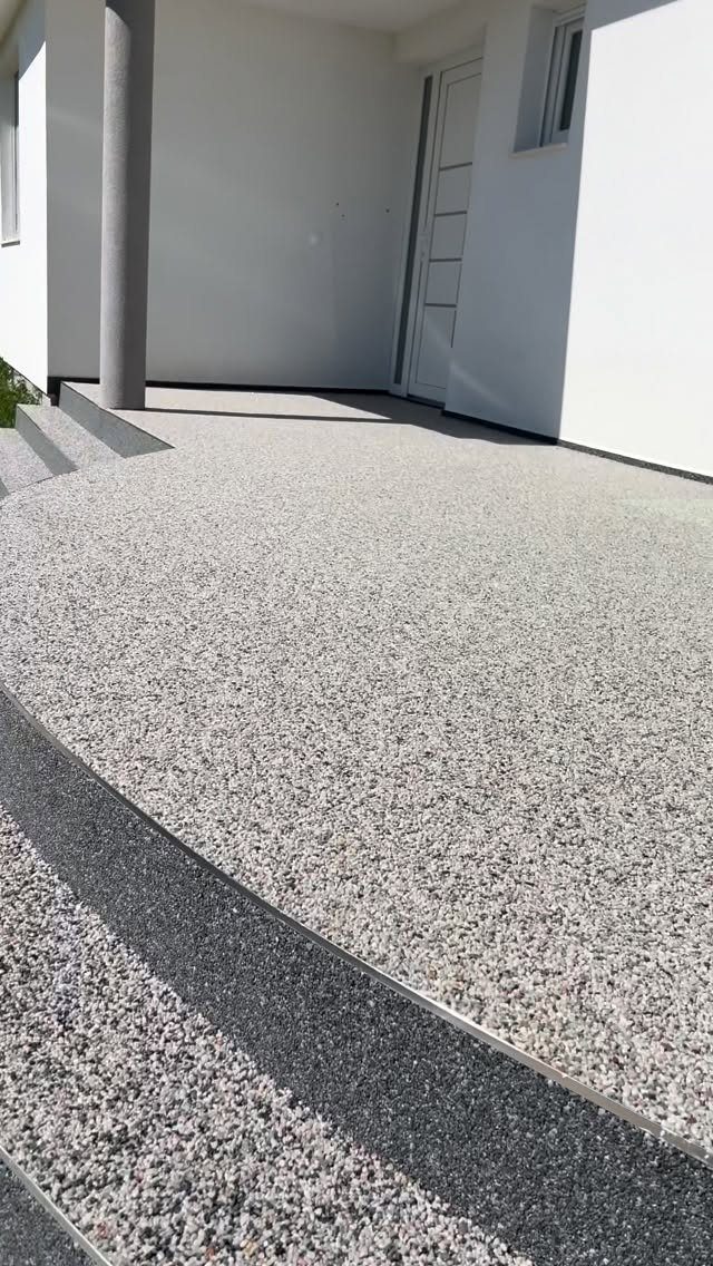 A seamless light grey aggregate stone patio with curved steps against a white building.