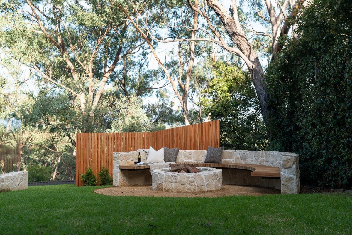 A circular stone fire pit surrounded by a curved stone and wood bench in a yard.