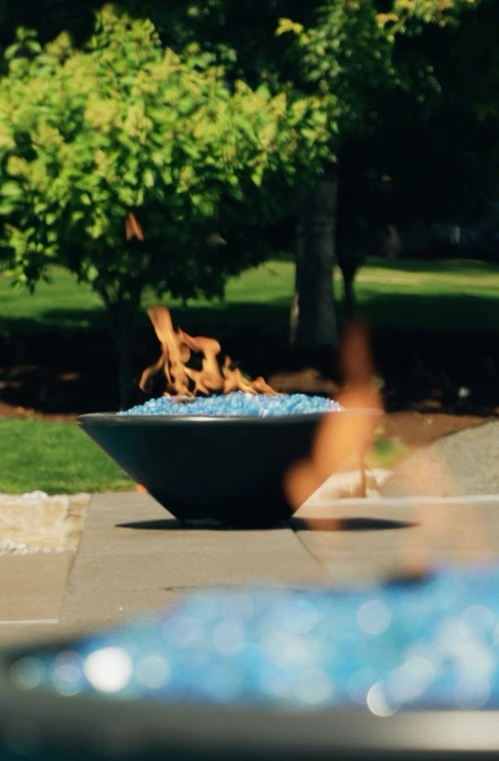 A black fire pit with blue glass beads and orange flames on a stone patio.