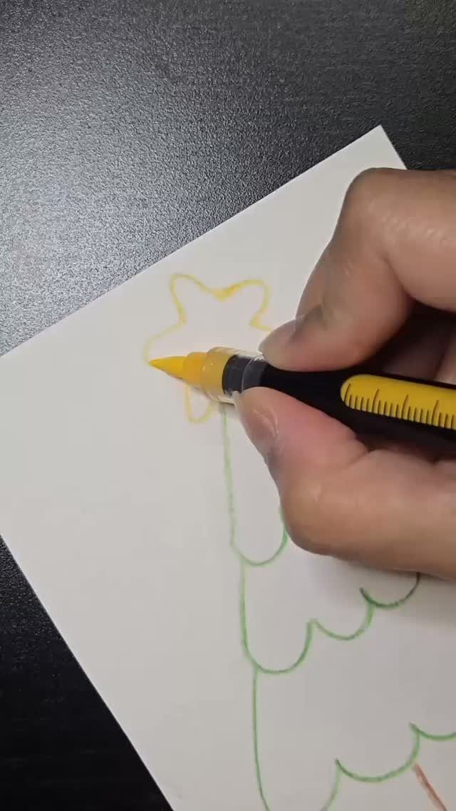 A hand coloring a yellow star on a Christmas tree outline with a marker.