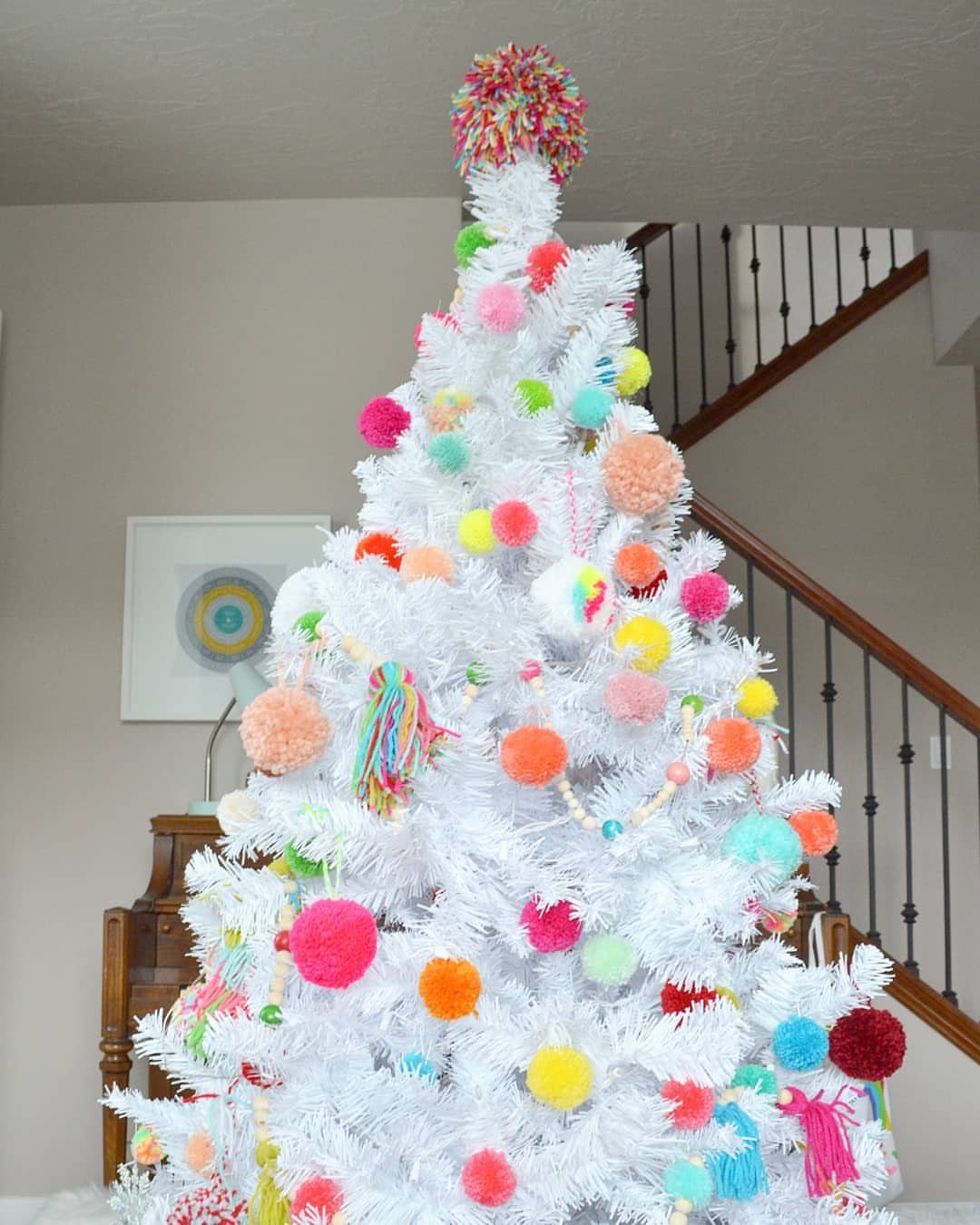 A white Christmas tree decorated with many bright, colorful pom-poms and a large pom-pom topper.
