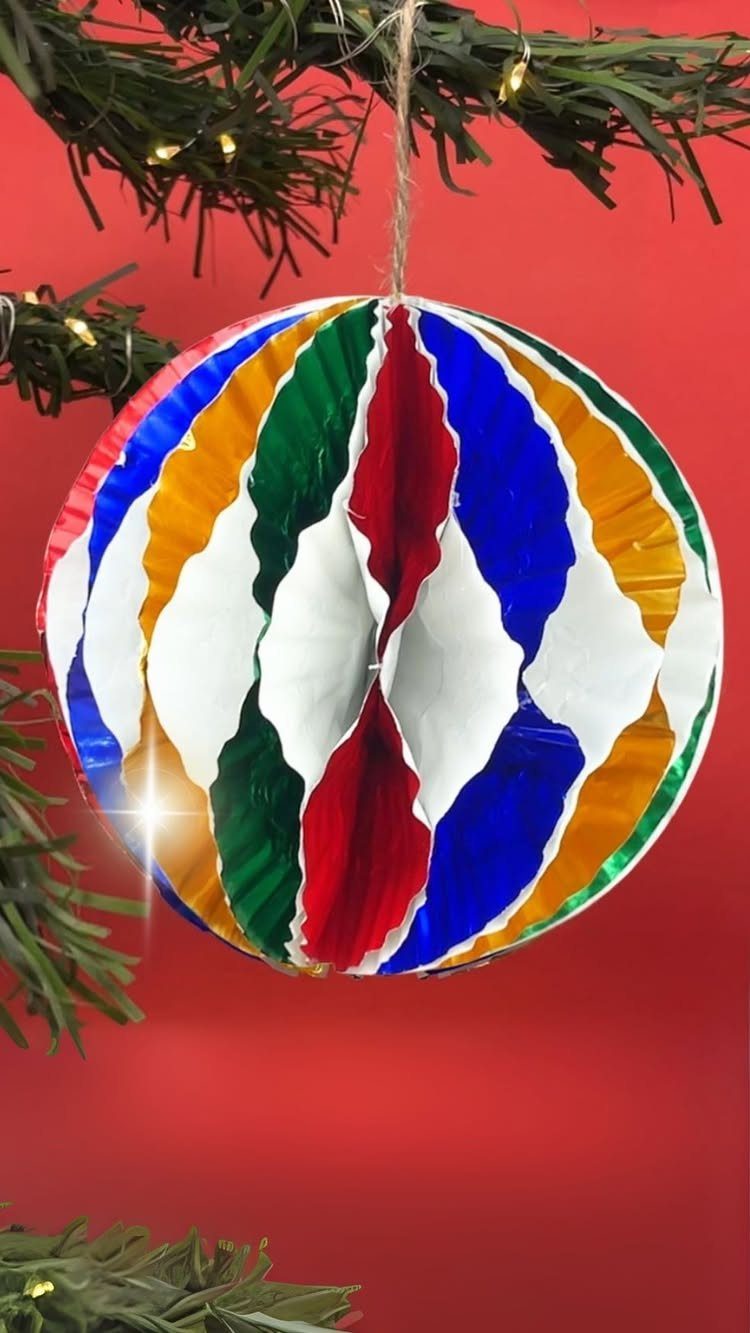 A colorful cupcake liner ornament hanging from a green Christmas tree branch.