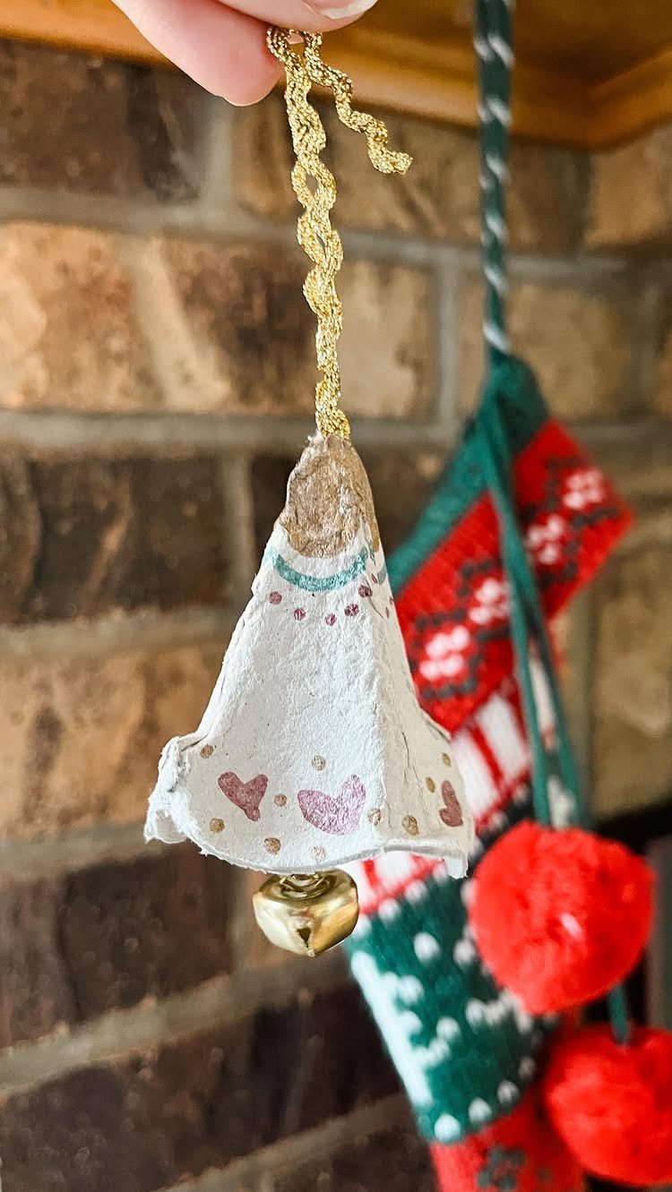 A decorated egg carton bell ornament with a small gold jingle bell hanging below it.