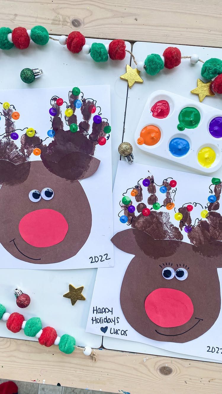 Two reindeer handprint crafts with colorful fingerprint lights on their antlers on a wooden table.