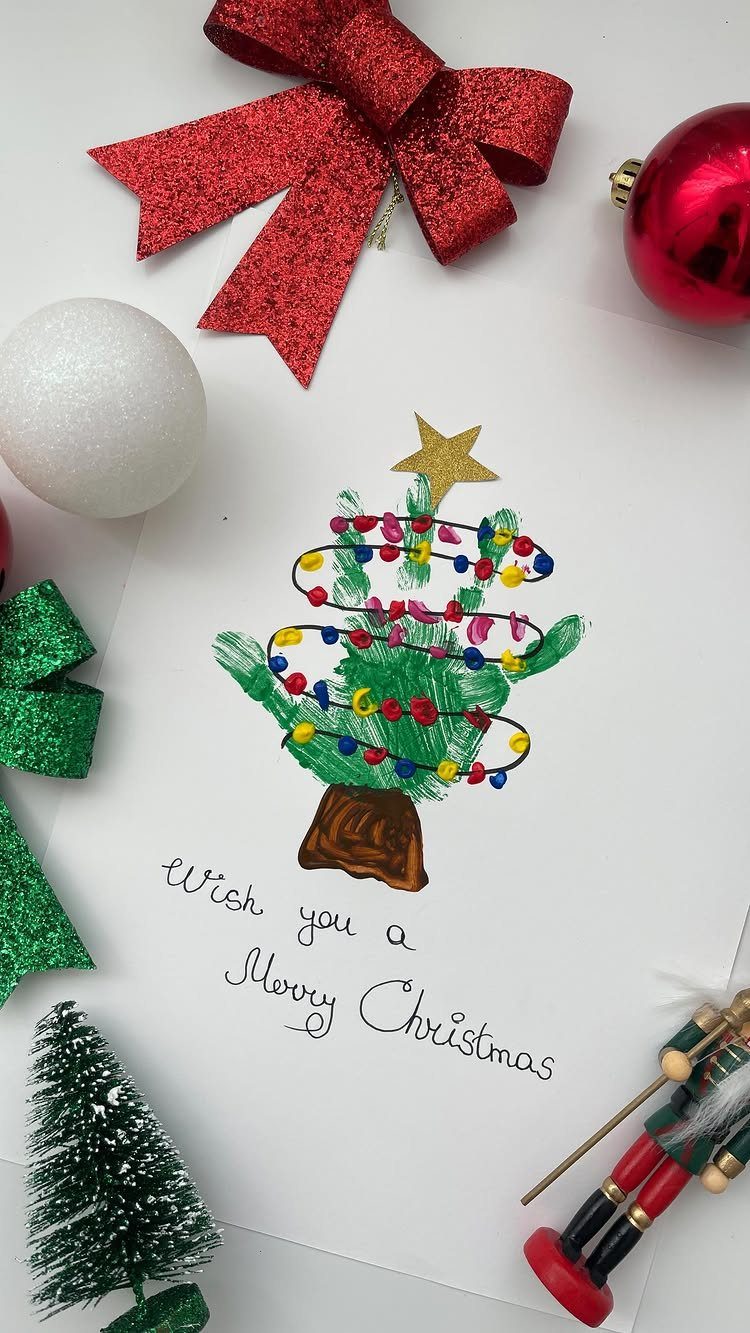 Handprint Christmas tree art on a card surrounded by festive red and green decorations.