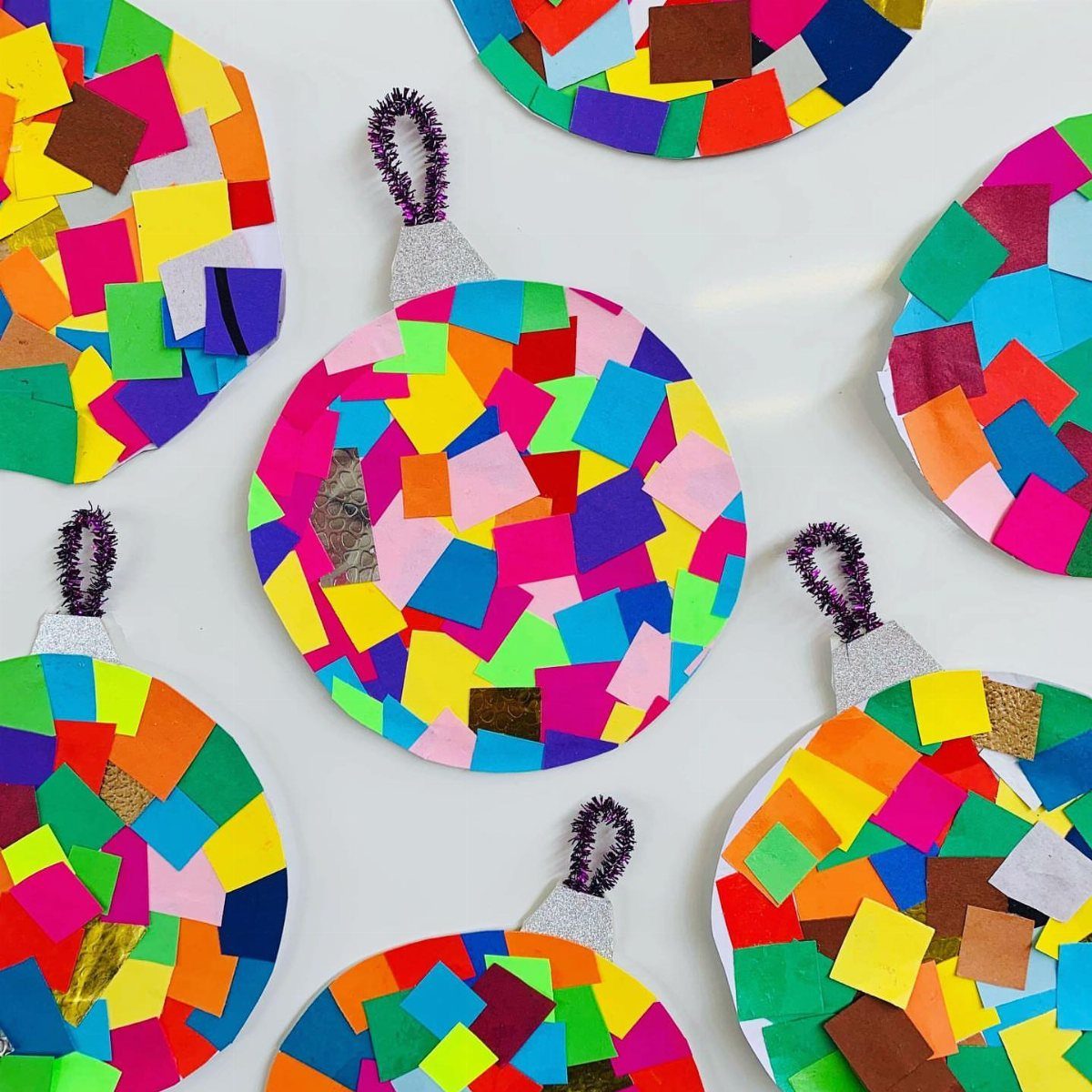 Colorful paper plate baubles decorated with bright scraps of tissue paper and felt on a white background.