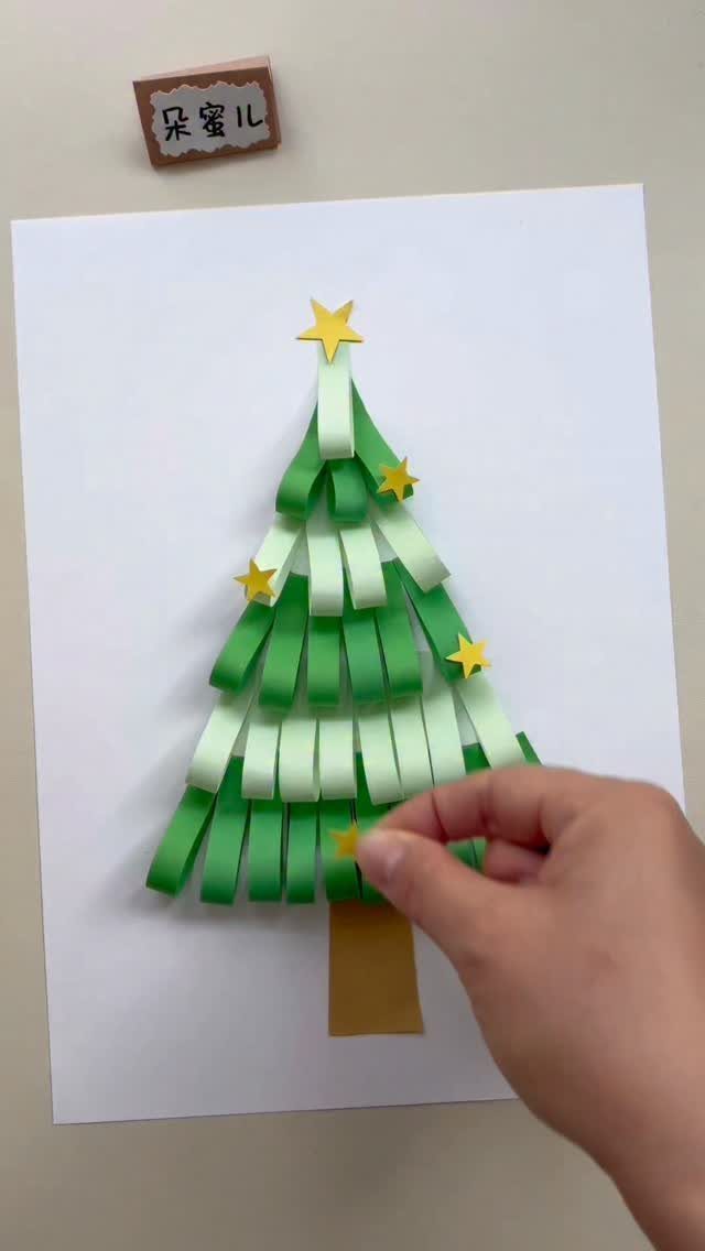 A hand placing a yellow star on a Christmas tree made of green paper strips.