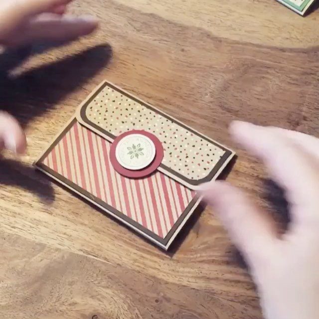 Hands holding a handmade striped and polka-dot paper gift card purse on a wooden table.