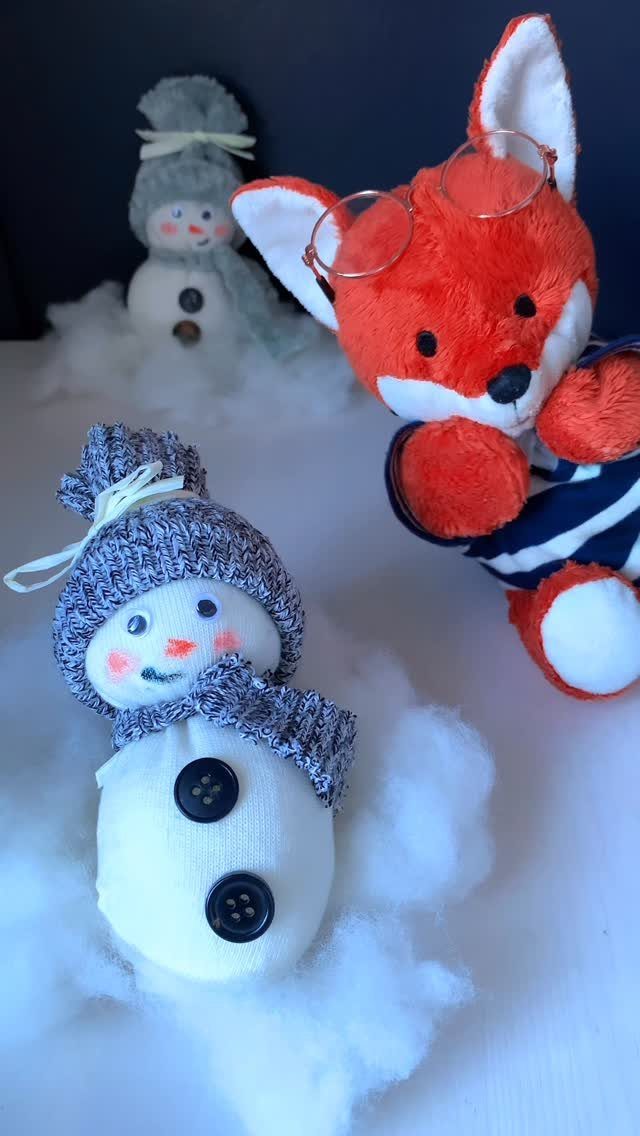 Handmade plush sock snowmen and an orange fox toy sitting on white fluffy cotton.