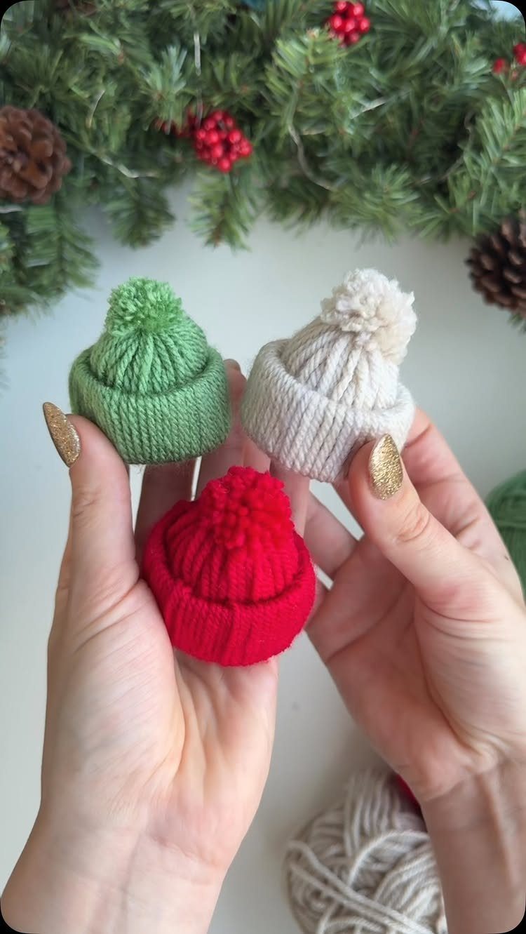 Hands holding three miniature knitted beanies in red, green, and white colors.