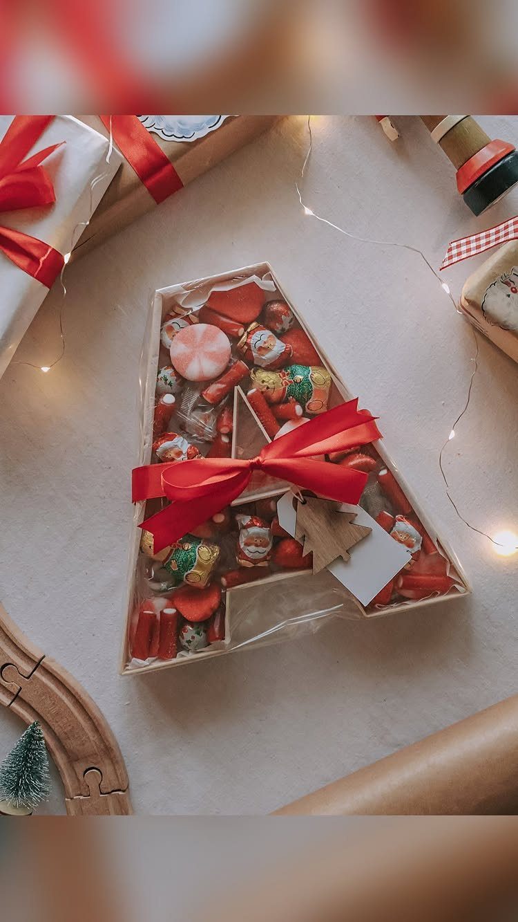A clear letter-shaped treat box filled with colorful candies and tied with a red ribbon.