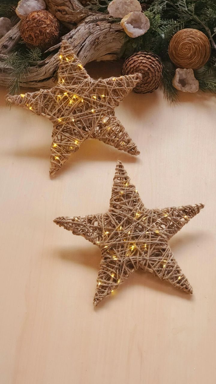 Two woven twine stars with warm fairy lights resting on a light wooden surface.