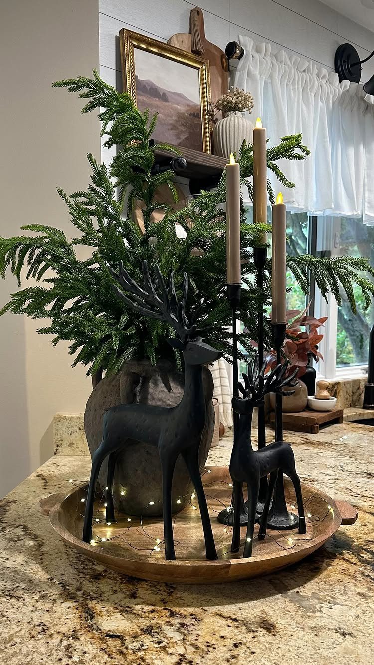 Black deer figurines and evergreen branches arranged in a wooden tray on a granite countertop.