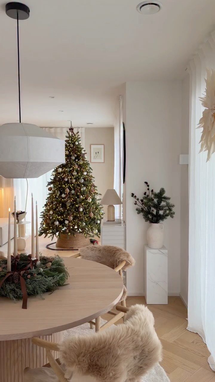 A decorated Christmas tree and dining table with greenery in a bright, modern interior.