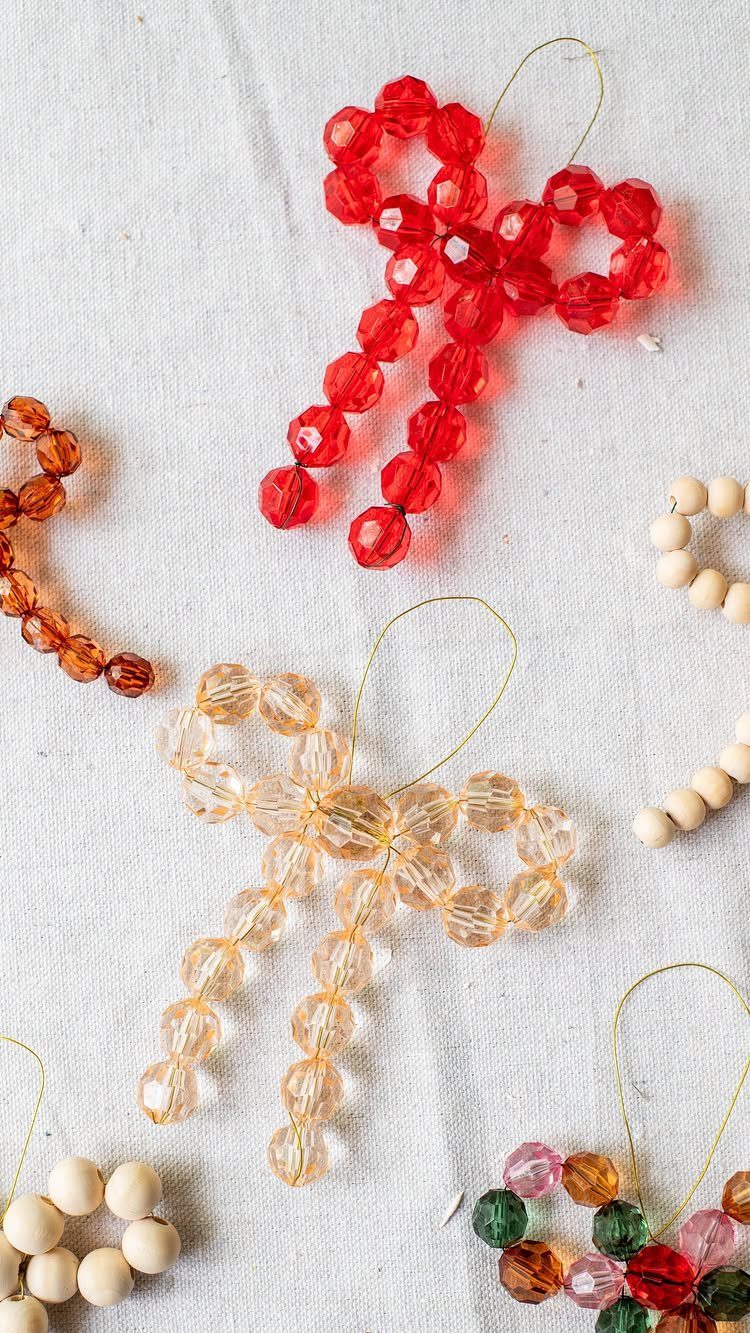 Beaded bow ornaments in red and peach colors resting on a white cloth surface.