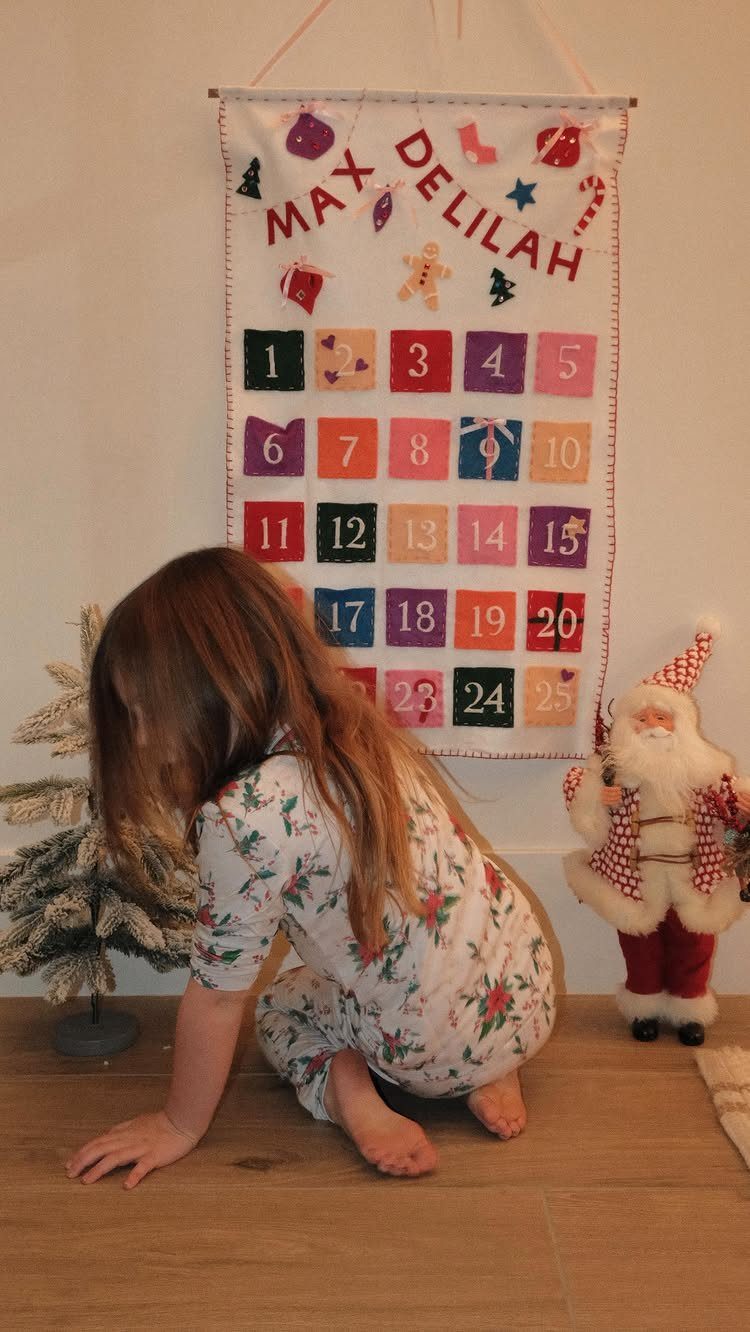 A young child in floral pajamas crawls on the floor near a colorful fabric advent calendar.