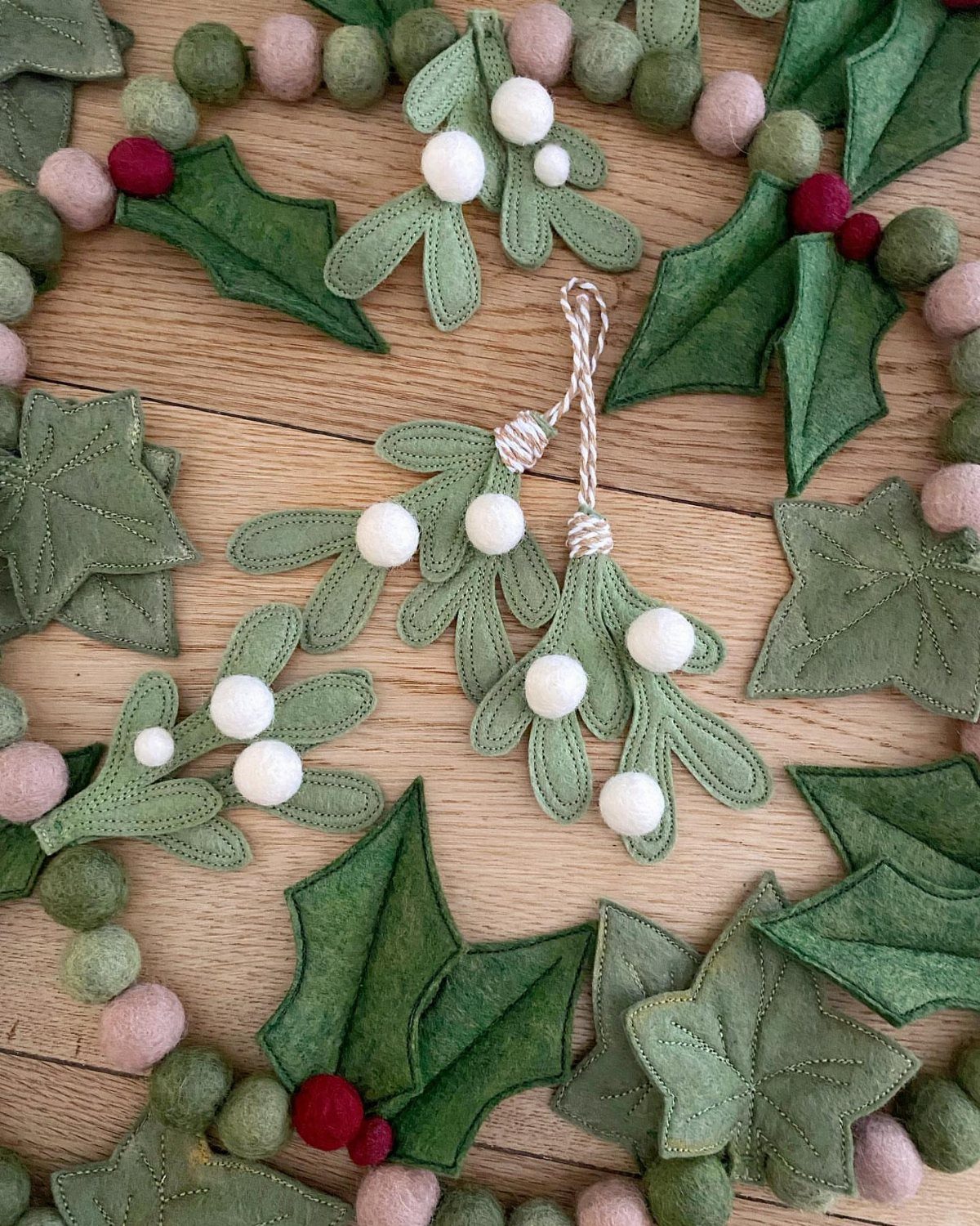 Felt holly leaf garland with red and white berries on a wooden background.