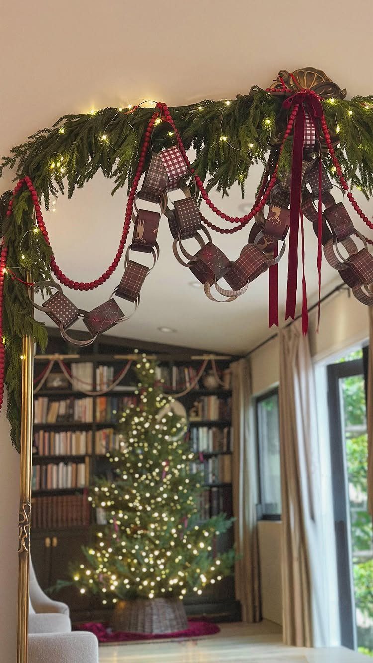 Evergreen garland with red beads and patterned paper chain loops hanging above a doorway.