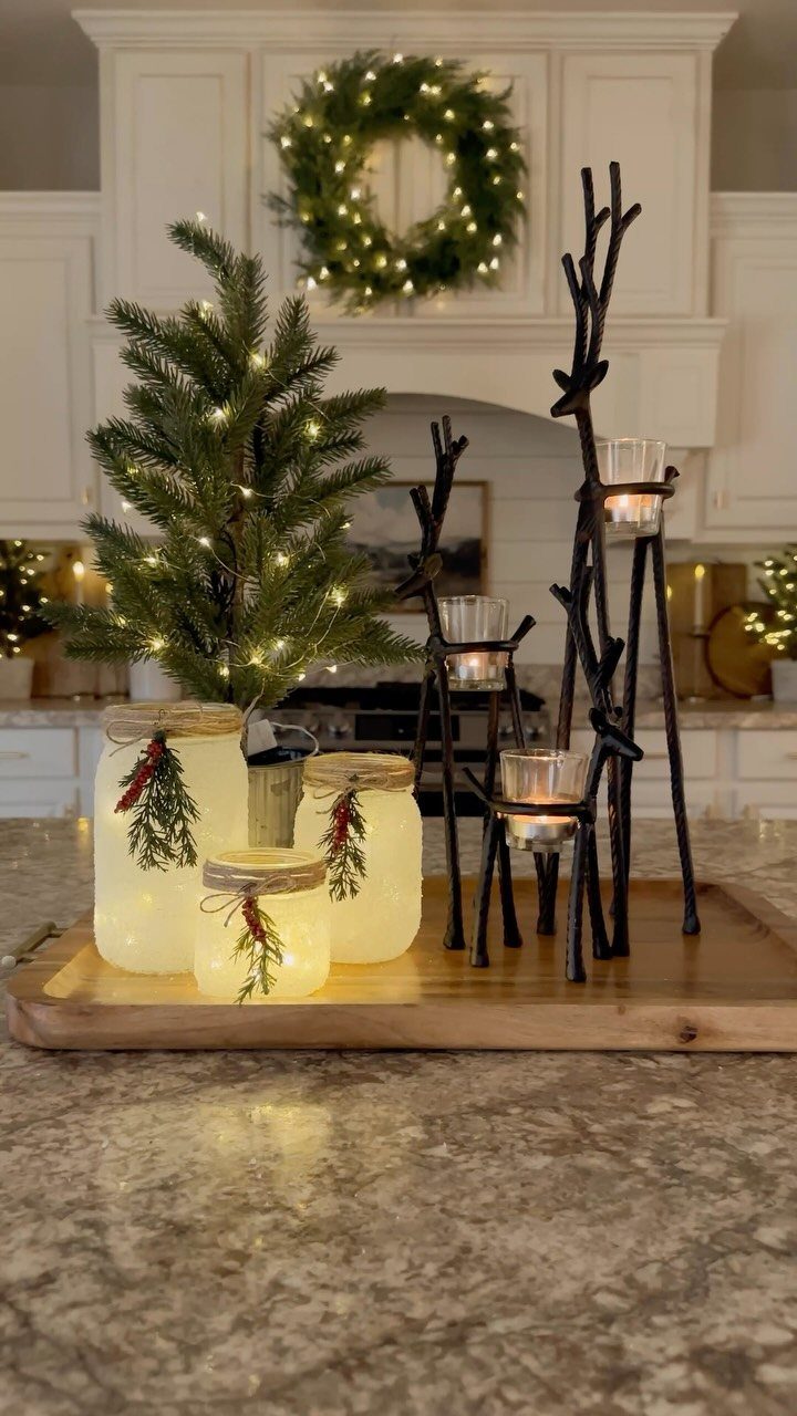 Frosted mason jar luminaries with greenery and red ribbon on a wooden tray.