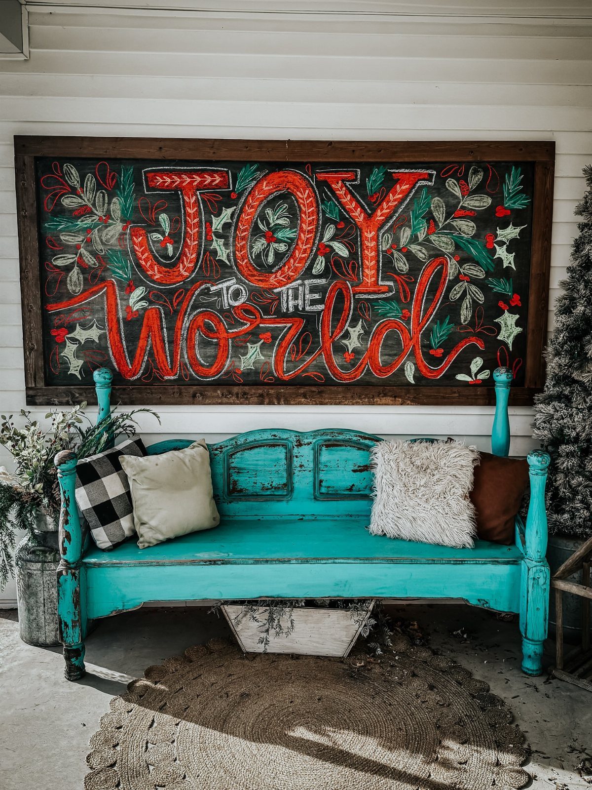 Large rustic wooden sign with red joyful lettering hanging above a turquoise vintage bench.