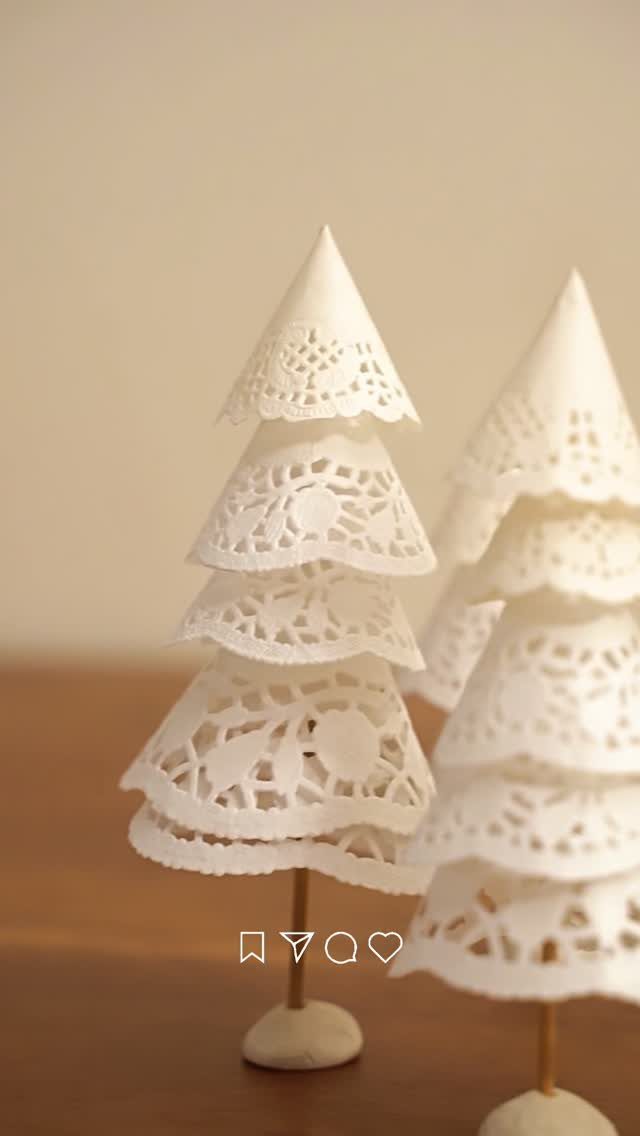 Two white decorative Christmas trees crafted from layered, intricate paper doilies on wooden stands.
