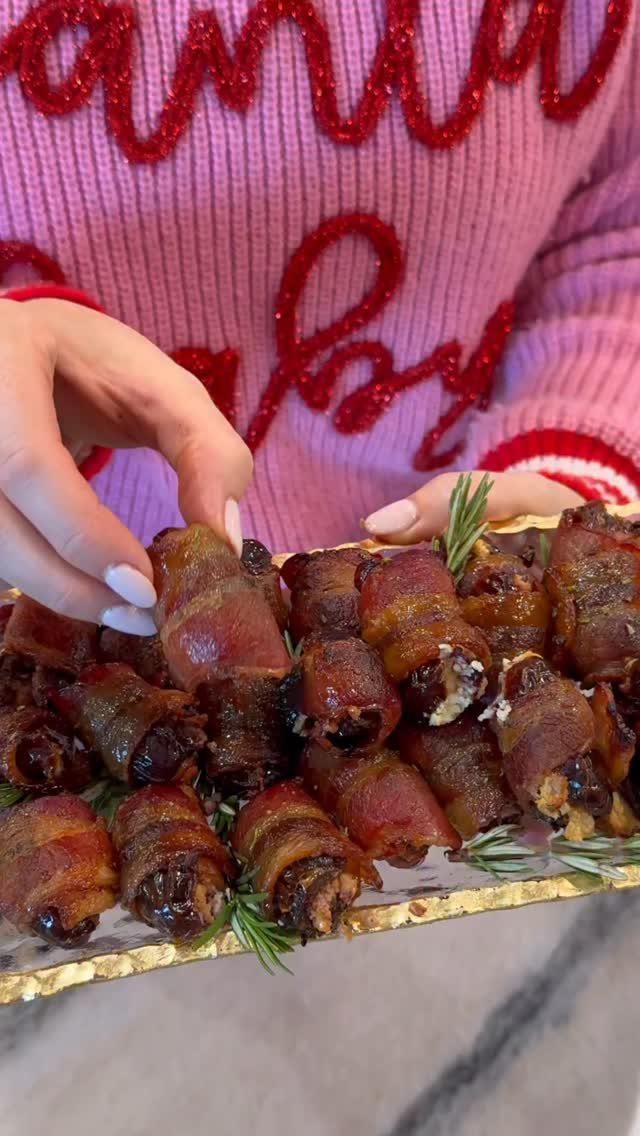 A hand reaches for bacon wrapped dates on a gold platter with rosemary sprigs.