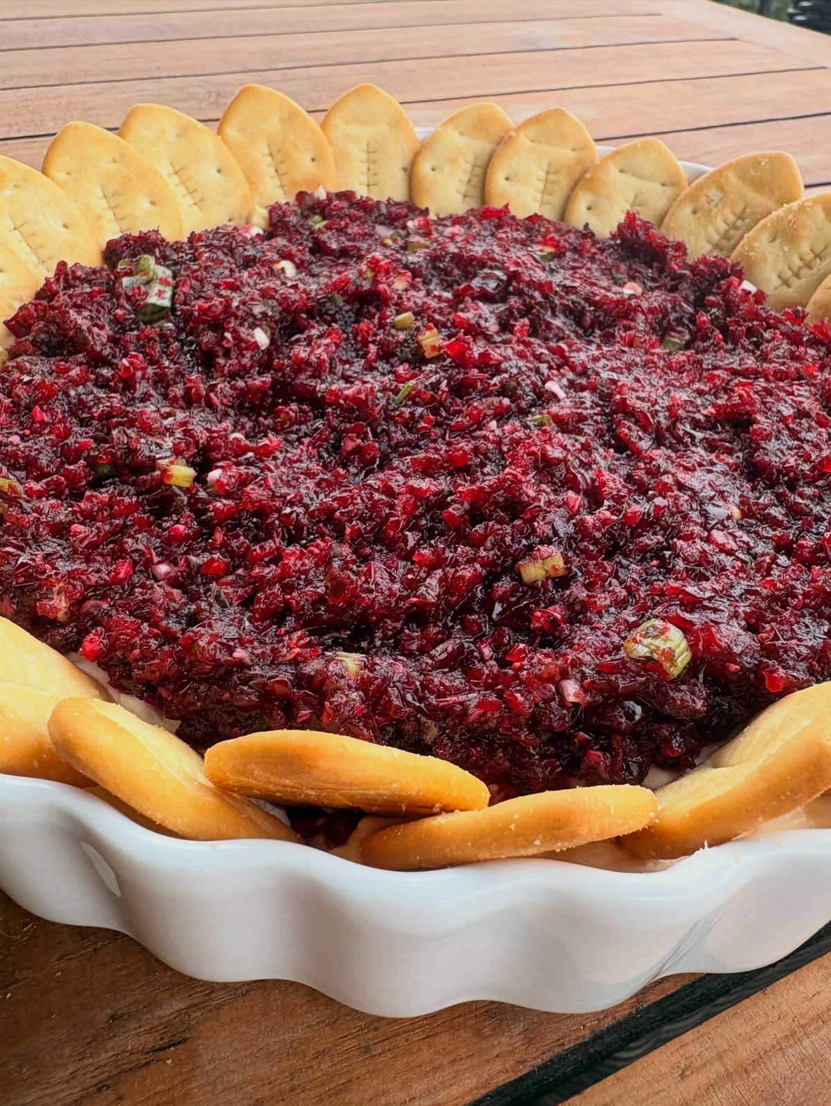 Red cranberry jalapeno dip surrounded by golden crackers in a white scalloped bowl.