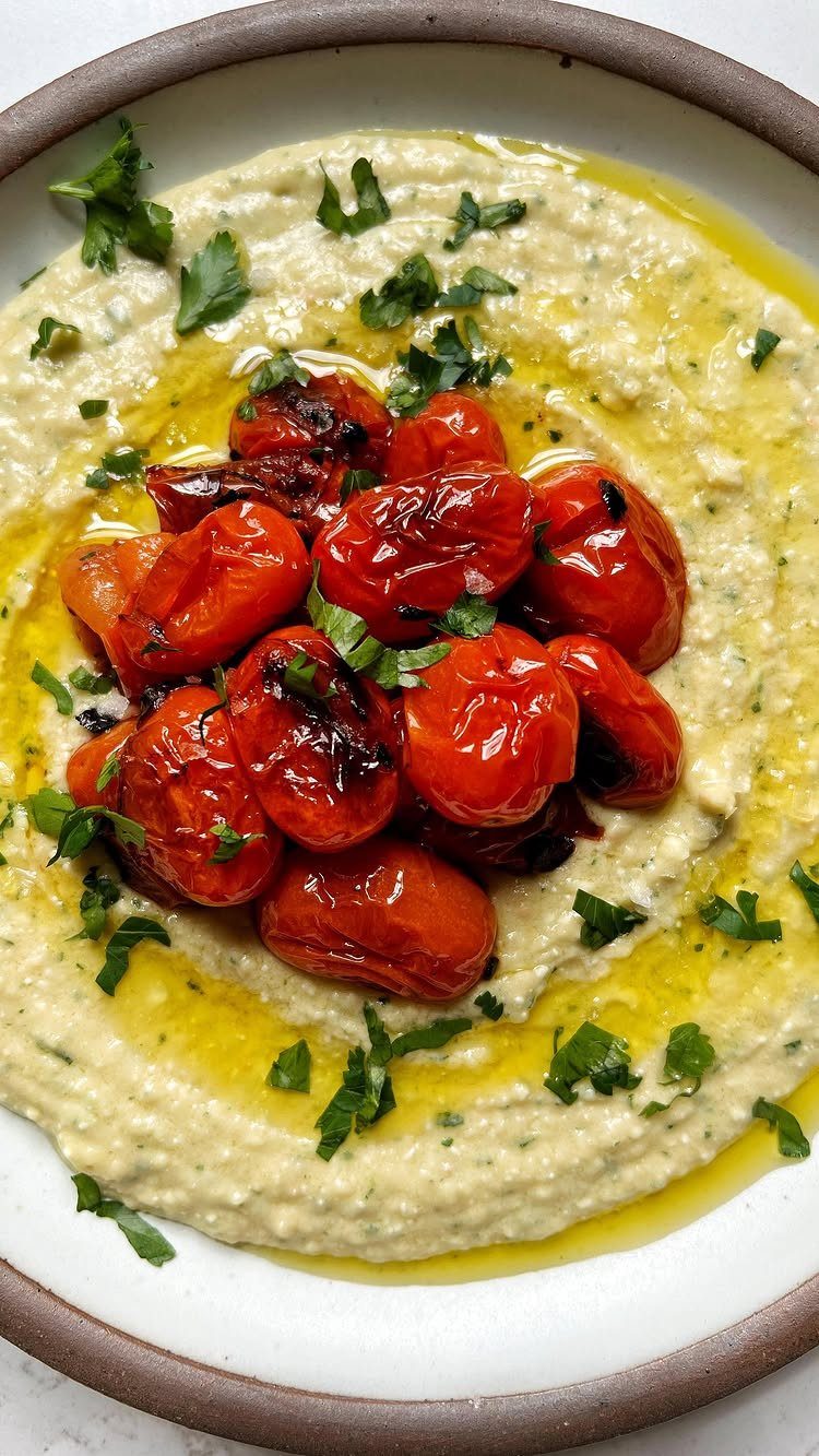 Creamy white bean dip topped with roasted cherry tomatoes and fresh parsley in a shallow bowl.