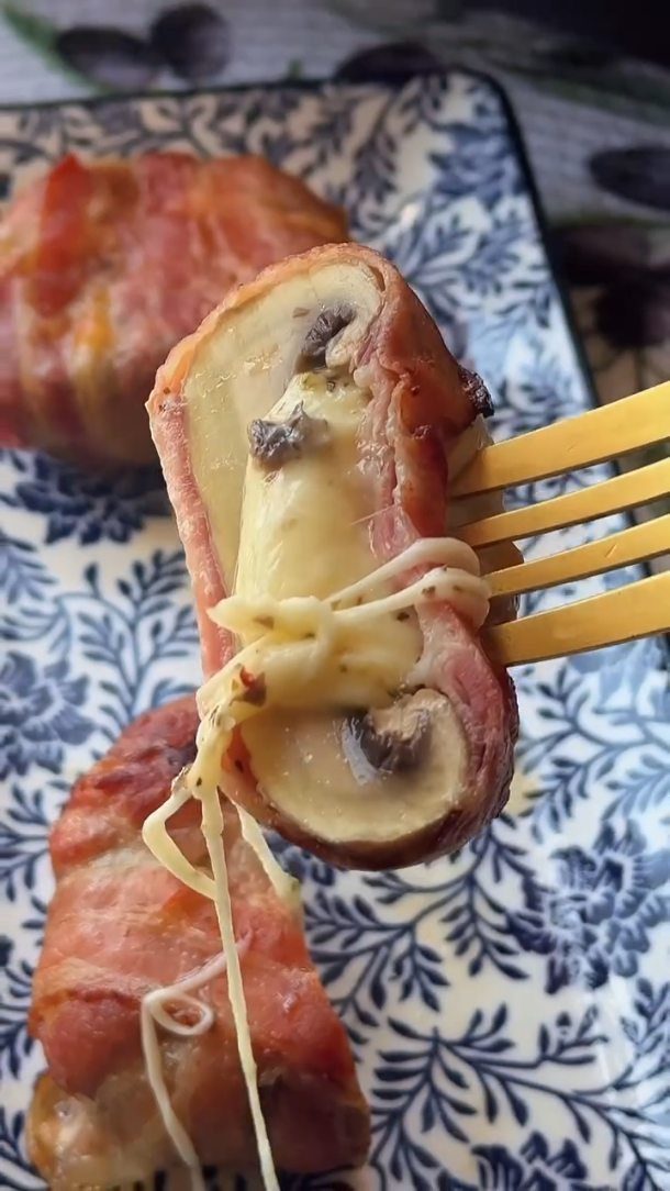 Bacon wrapped stuffed mushroom with melted cheese being lifted by a gold fork.