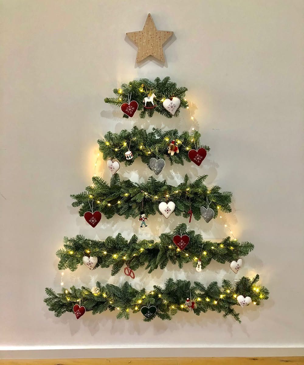 8 Christmas Tree Wall Ideas: String Lights to Pallet Builds 3 Evergreen branches arranged on a wall in a Christmas tree shape with lights and ornaments.