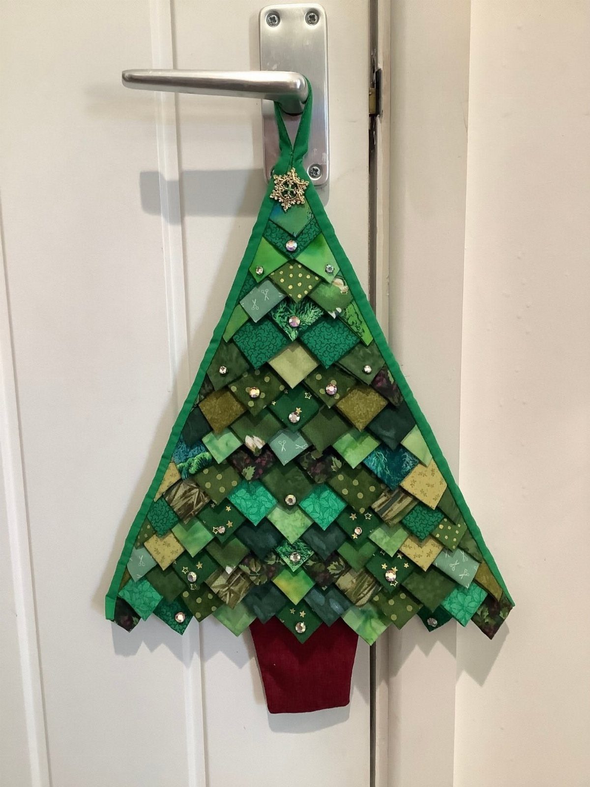 8 Christmas Tree Wall Ideas: String Lights to Pallet Builds 6 A green fabric patchwork Christmas tree hanging from a white door handle.