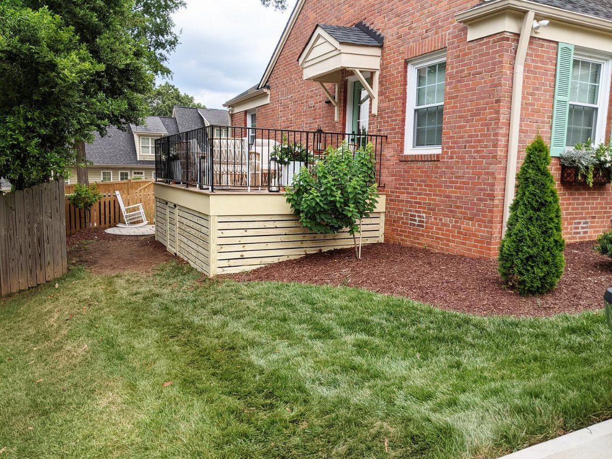 Composite Deck Skirting: 5 Ideas That Close the Gap 1 A wooden deck featuring horizontal slat skirting installed against a red brick house.