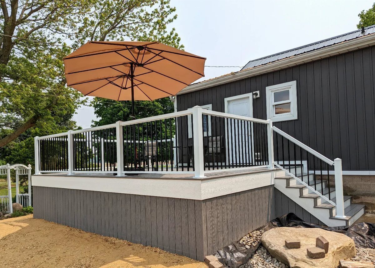Composite Deck Skirting: 5 Ideas That Close the Gap 4 A grey composite deck with white railings and solid grey skirting panels next to a dark house.