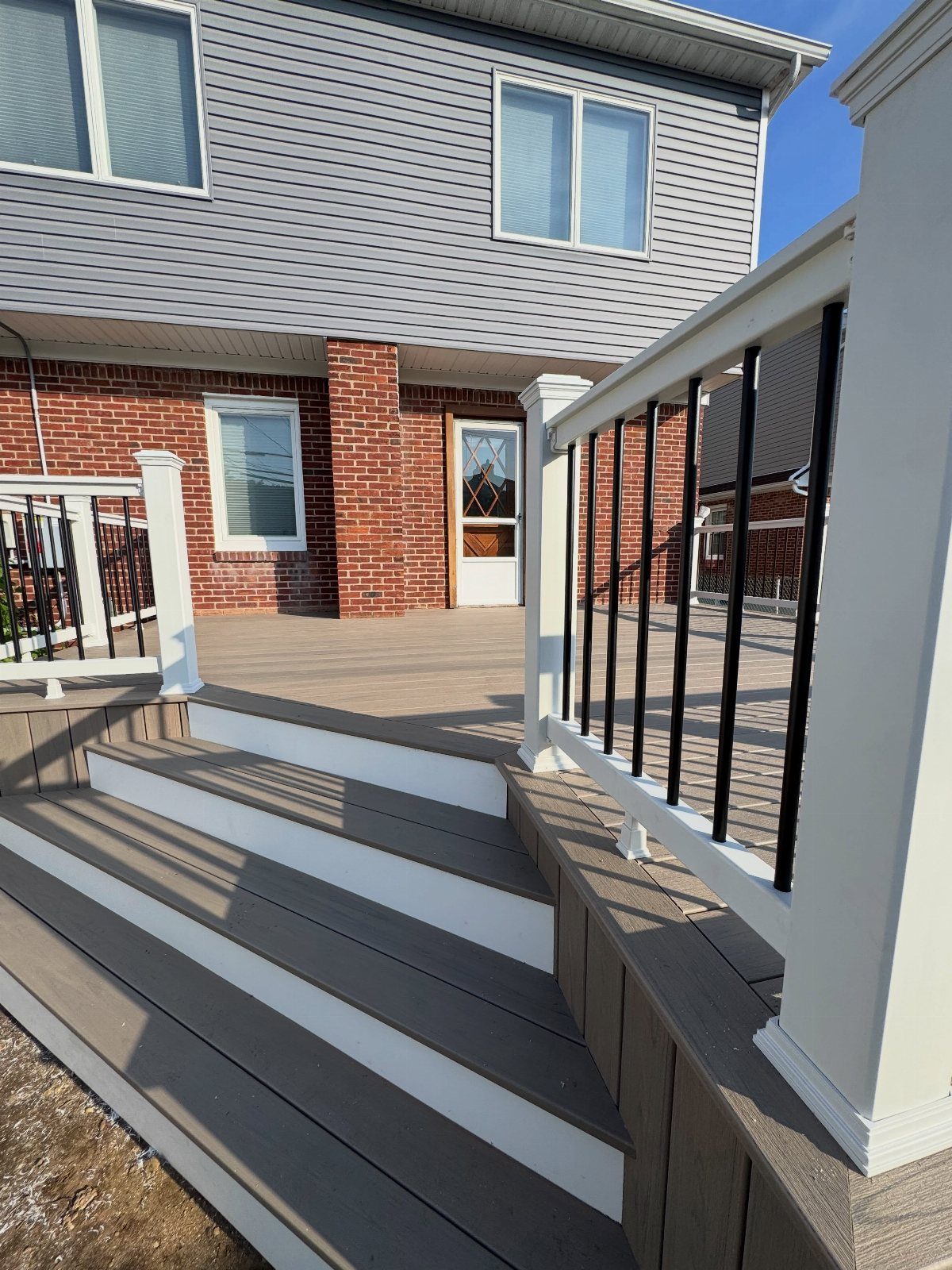 Composite Deck Skirting: 5 Ideas That Close the Gap 3 A finished composite deck with white railings and grey steps against a brick and siding house.