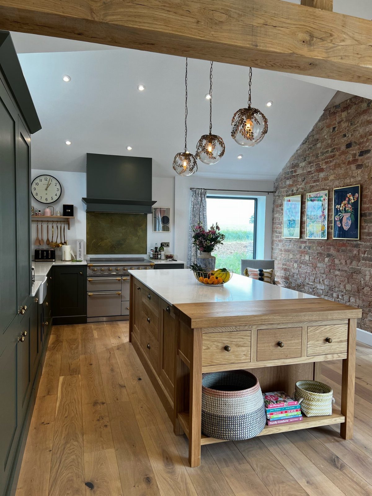 A modern kitchen with a wooden island, dark cabinetry, and an exposed brick wall.