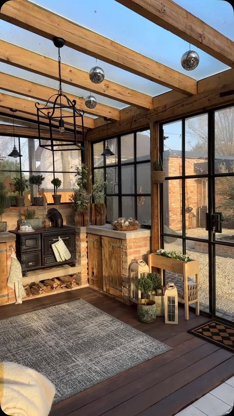 Rustic kitchen with wooden beams, glass ceiling, black stove, and large windows overlooking a courtyard.