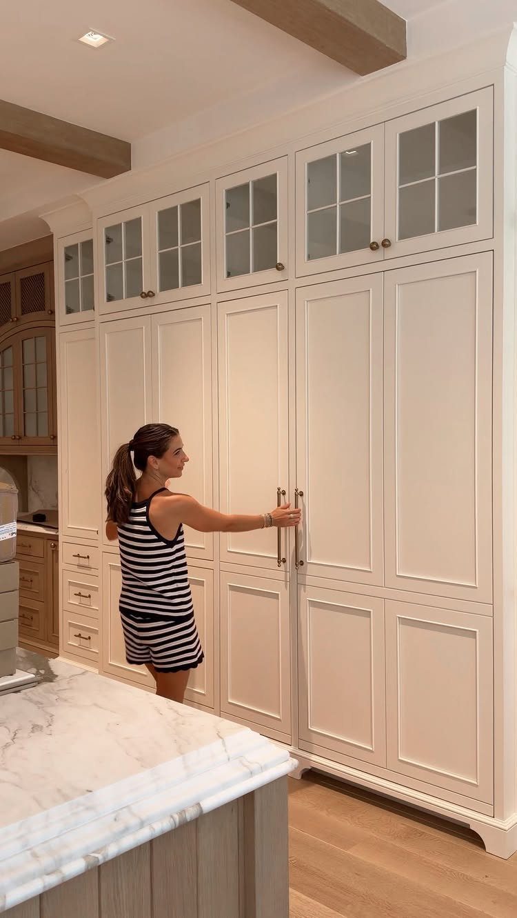 A woman opening large white built-in kitchen cabinets with long metal handles in a bright room.