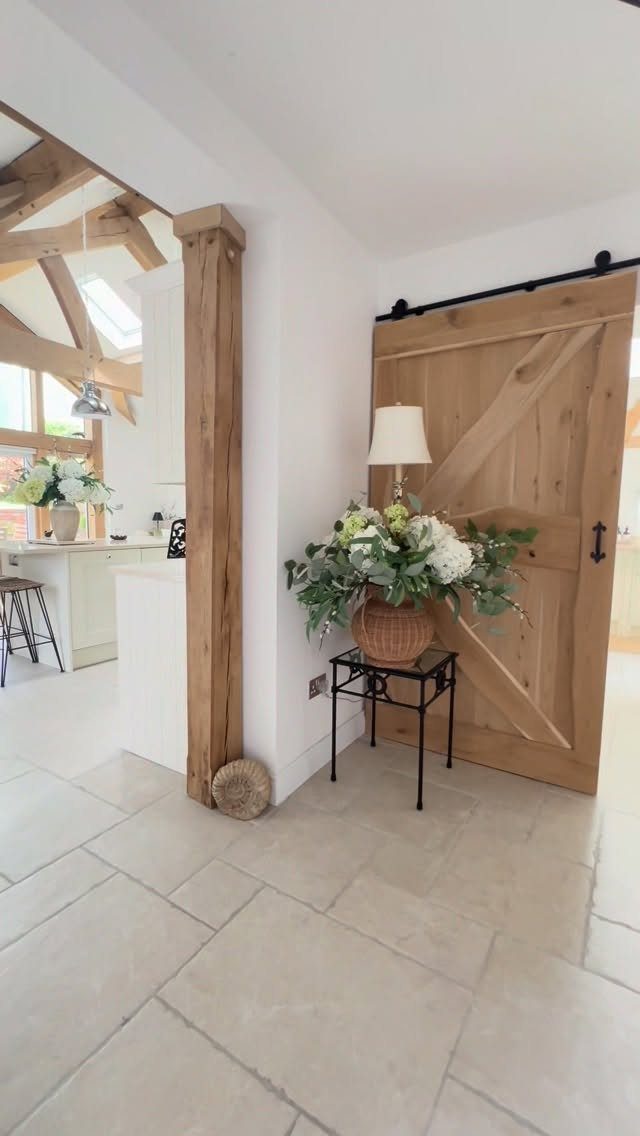 A wooden sliding barn door stands next to a small table with flowers in a bright room.