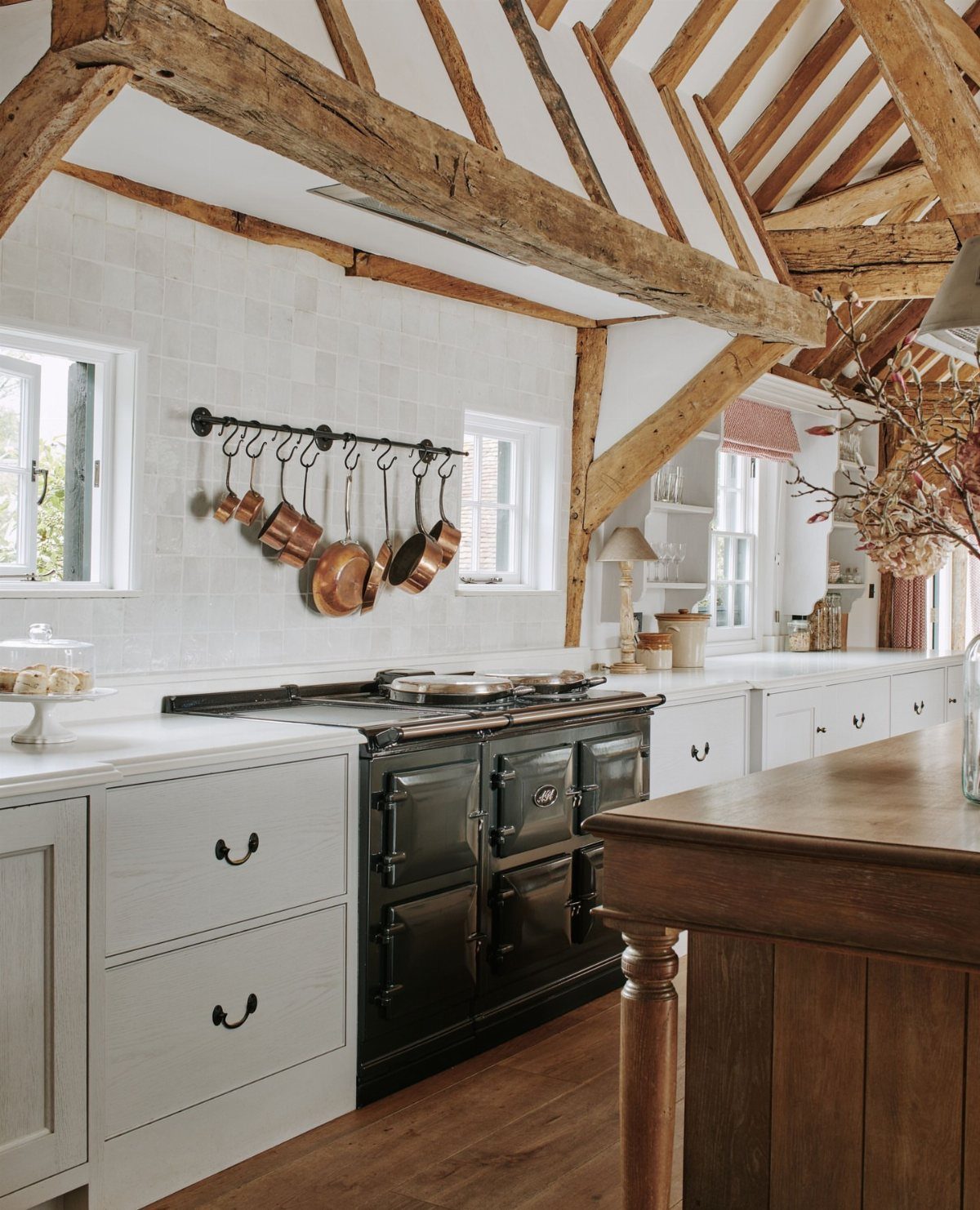 Rustic kitchen with exposed wooden beams, white cabinets, and a large black vintage range cooker.