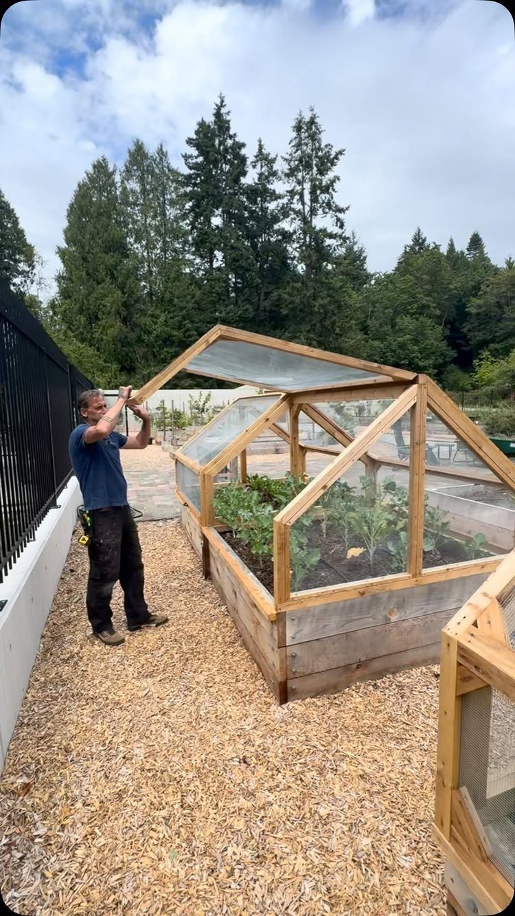 25 Creative and Gardening Ideas for Backyards Big or Small 3 A man building a wooden greenhouse structure containing green plants in a garden.