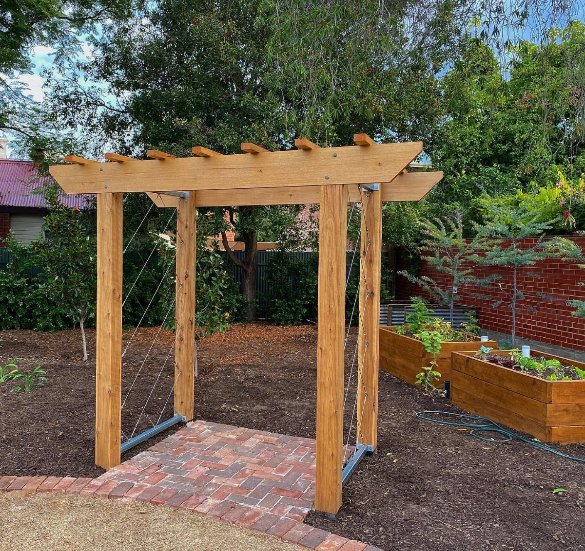 25 Creative and Gardening Ideas for Backyards Big or Small 9 A wooden garden arbor structure standing over a red brick walkway in a backyard.